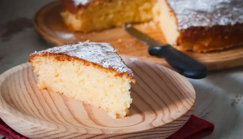 Una fetta di torta all'acqua soffice e spolverata di zucchero a velo su un piatto di legno.