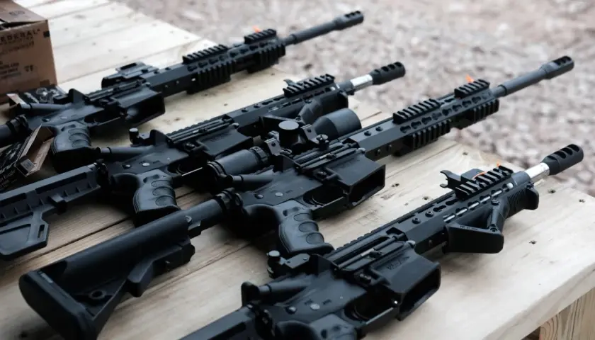 Kilka karabinów AR15 leży na drewnianym stole. W tle widać pudełko z amunicją.