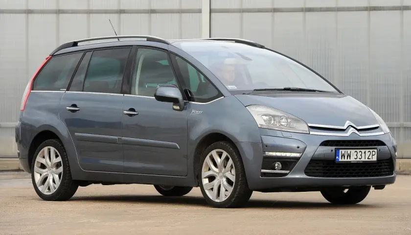 Szary Citroen C4 Grand Picasso 2.0 HDI z kierowcą za kierownicą, zaparkowany przed budynkiem.