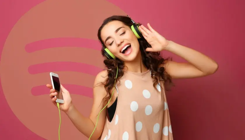 Dziewczyna z słuchawkami na uszach i telefonem w dłoni, ciesząca się muzyką. Idealna okazja, by sprawdzić Spotify Premium za 0,99!