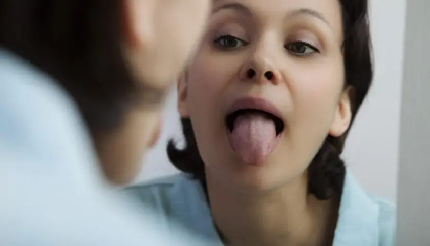 Donna si guarda allo specchio, mostrando la lingua. La saliva aiuta a digerire e a mantenere la bocca sana.