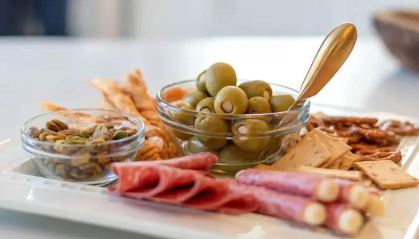 Plateau apéro raclette : olives, pistaches, salami, bretzels et crackers. Parfait pour un moment convivial.