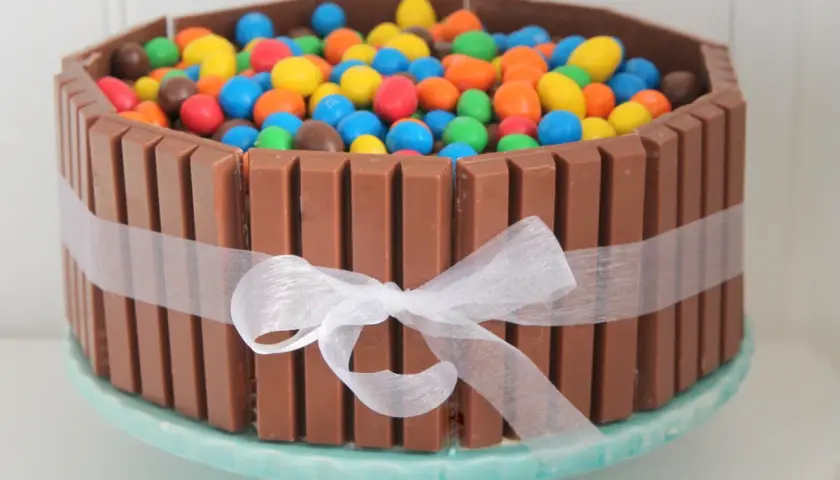 En färgglad KitKat tårta fylld med M&M's, omgiven av KitKat-bars och ett vitt sidenband. En dröm för alla godisälskare!