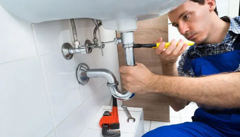 Monter instalacji sanitarnych dokręca kluczem syfon pod umywalką.