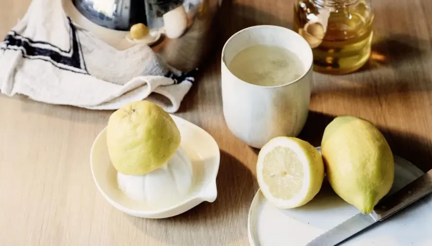 Zitronentee bei Halsschmerzen: frische Zitronen, ein Glas Tee und Honig auf einem Holztisch.
