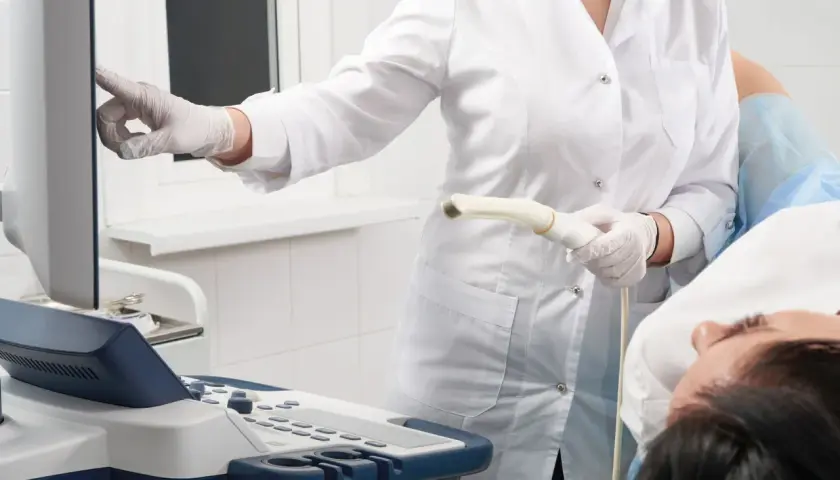 Arzt führt eine Untersuchung mit einem Ultraschallgerät durch. Die Patientin liegt auf dem Tisch.