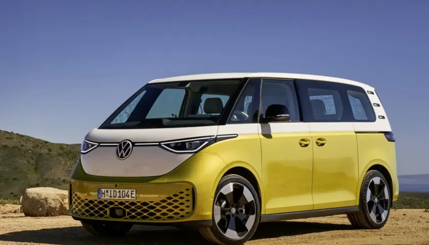Minivan elettrico Volkswagen ID. Buzz bicolore giallo e bianco, parcheggiato su un terreno sterrato con sfondo di colline e cielo azzurro.