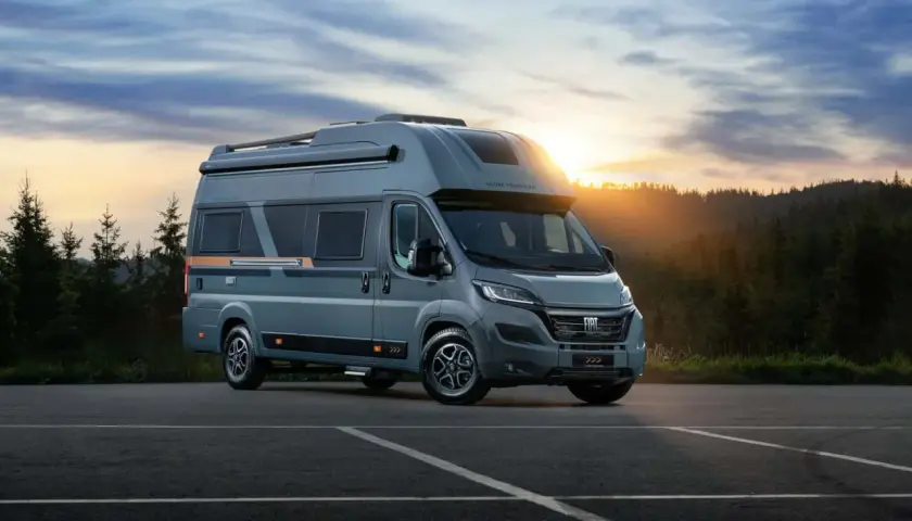Nowe kampery Globe Traveller zapraszają na przygodę. Szary Fiat Ducato z nowoczesnym designem na tle zachodzącego słońca i lasu.