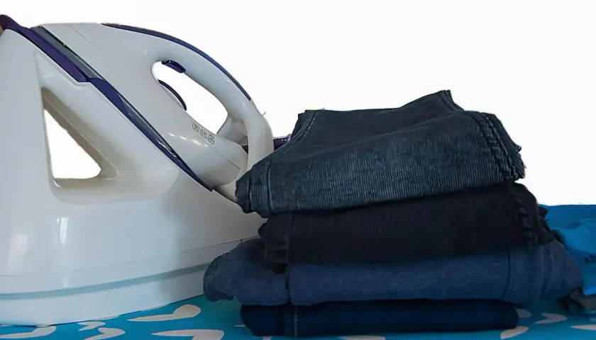 Fer à repasser et pile de vêtements sombres sur une planche à repasser. Apprenez comment repasser du polyester pour un résultat impeccable.