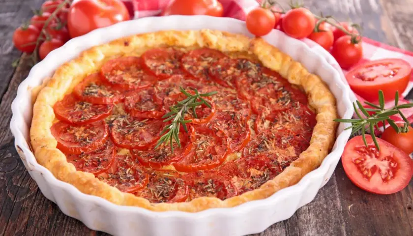 Tarte aux tomates fraîches, garnie d'herbes et d'une branche de romarin. Un accompagnement tarte tomate parfait pour un repas d'été.
