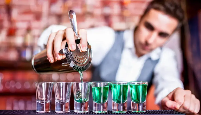 Barman nalewa zielony shot do kieliszków. Zastanawiasz się, ile zarabia barman na godzinę?