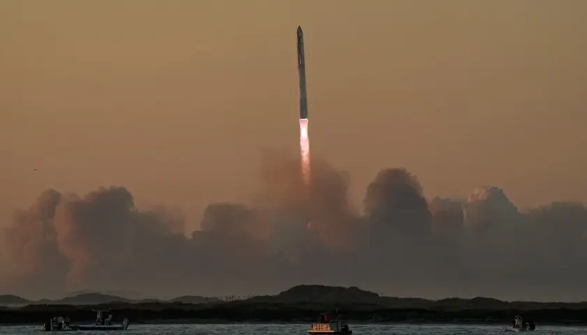 Starship start. Rakieta wznosi się w niebo, zostawiając za sobą kłęby dymu. Na wodzie widać łodzie obserwujące ten spektakularny widok.