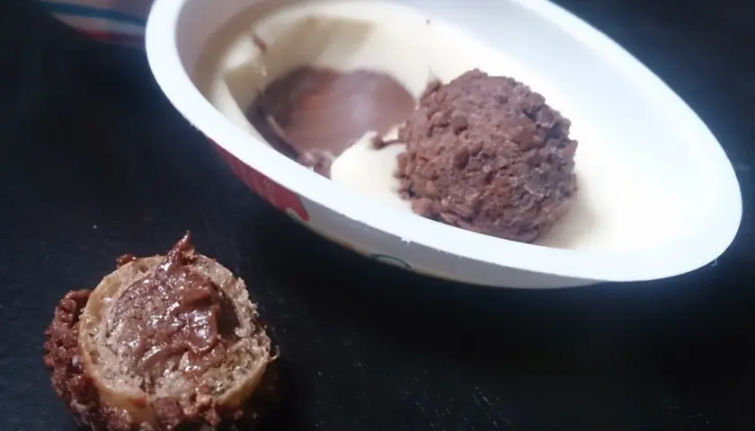 Lody Kinder Joy w białym opakowaniu z czekoladową kulką i kawałkiem waflowym z kremem.
