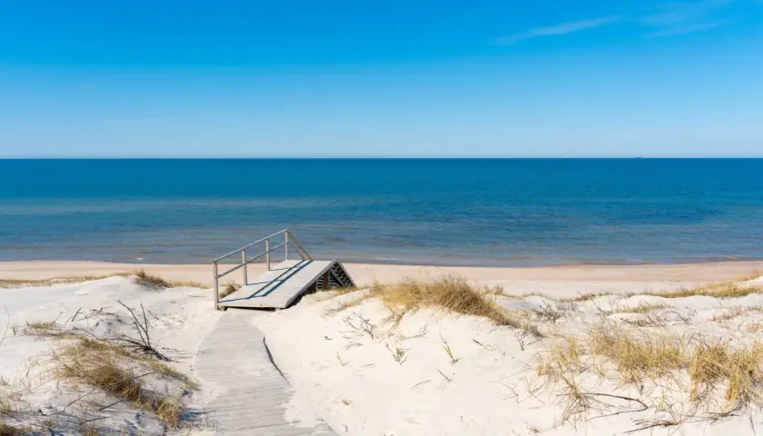 Drewniane schody prowadzą na piaszczystą stegna plaża. Błękitne morze i niebo tworzą spokojny krajobraz.