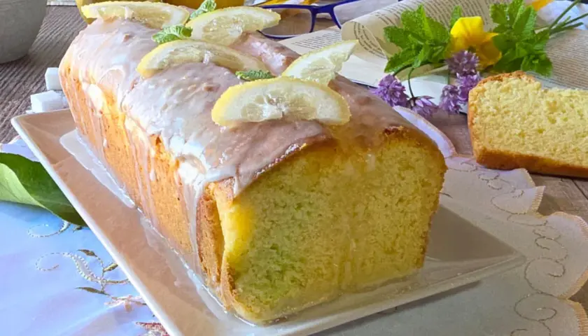Un delizioso plumcake al limone glassato, decorato con fette di limone e menta, pronto per essere gustato.