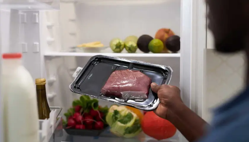 Un homme regarde un morceau de viande dans son emballage. Il se demande : viande hors frigo combien de temps ?