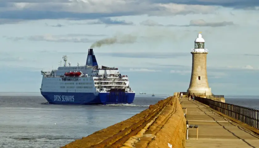 Duży prom DFDS Seaways wypływa z portu, kierując się na Bornholm. Obok stoi latarnia morska.