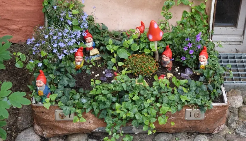 Ein alter Koffer dient als Blumenbeet. Gartenzwerge und rote Pilze bevölkern die üppige Bepflanzung.