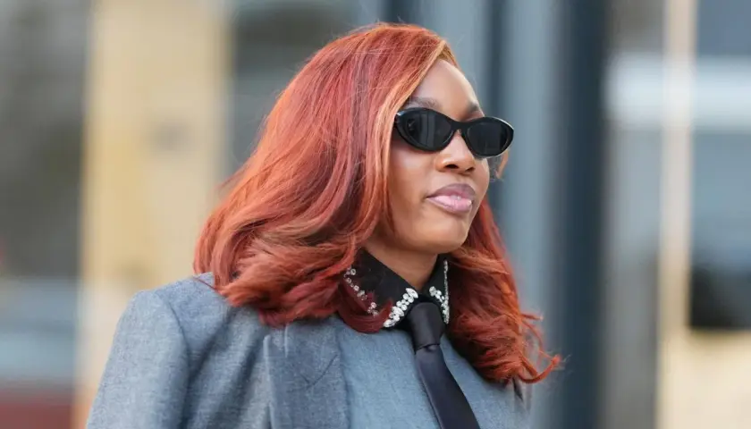 Feuerrote Haare, auffällige Sonnenbrille und ein Blazer – diese Frau verkörpert den Trend für Frisuren 2026.