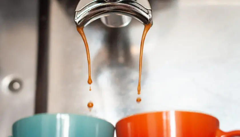 Gorące, aromatyczne espresso co to? Dwie strumienie kawy spływają do kolorowych filiżanek.