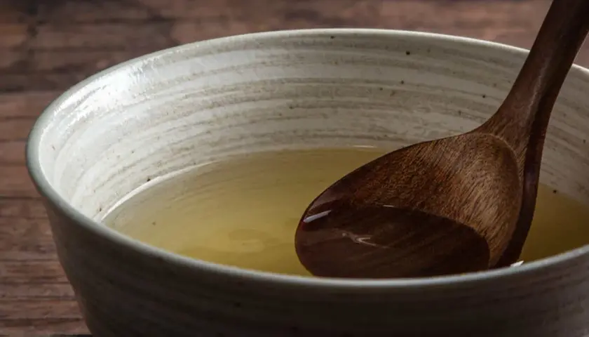 A wooden spoon rests in a bowl of clear, golden broth, hinting at the subtle flavors of various types of dashi.