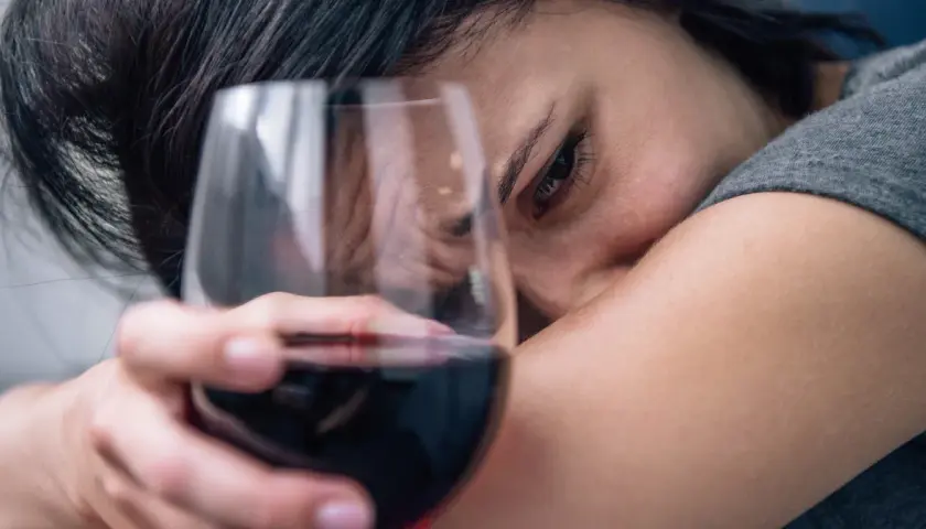 Smutna kobieta z kieliszkiem wina, symbolizująca 6 objawów uzależnienia od alkoholu.