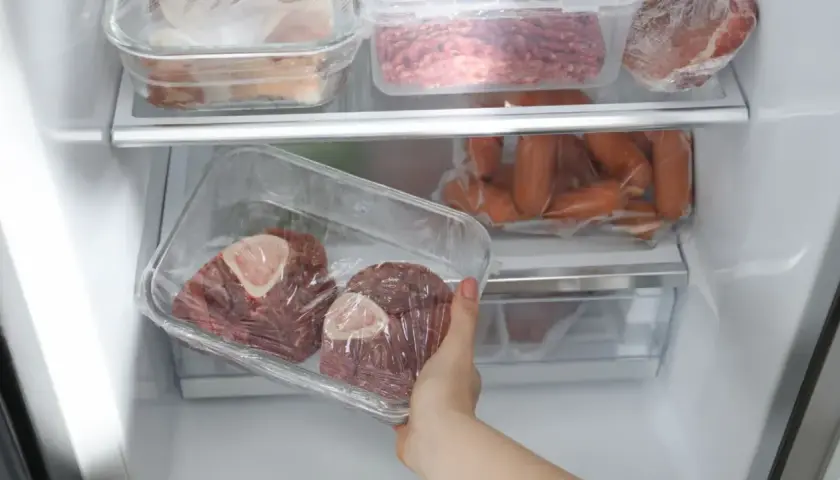 Main du réfrigérateur, deux morceaux de viande rouge avec os, emballés dans du film plastique. Viande cuite hors frigo 12h, risque de détérioration.
