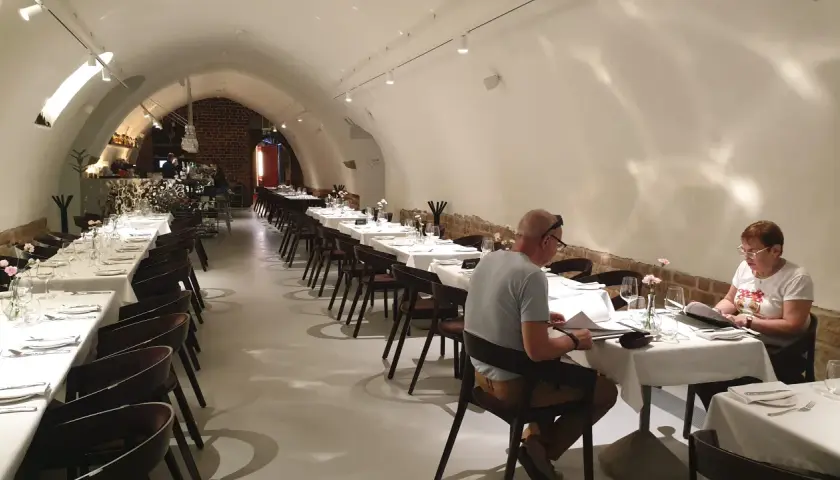 Elegancka sala restauracyjna z białymi obrusami i nakrytymi stołami. W tle bar. To może być najstarsza restauracja w Polsce.