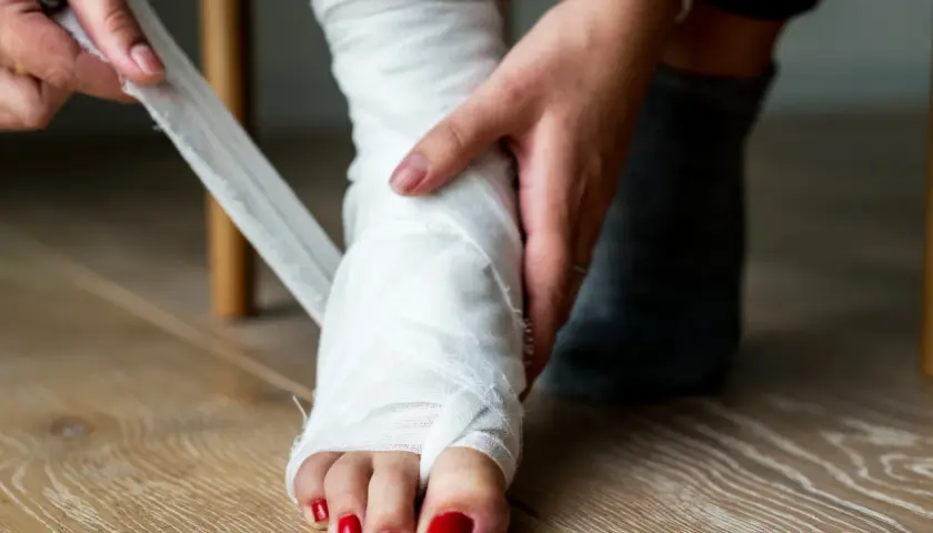 Osoba owija bandażem stopę po zwichniętej kostce.