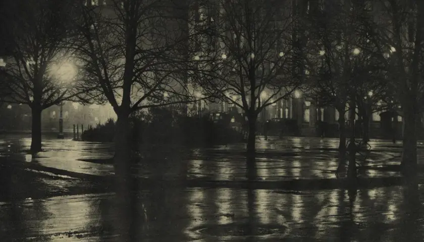 Nocny park, mokre alejki odbijające światła latarni i okien. Piktorializm w fotografii oddaje nastrój i atmosferę.
