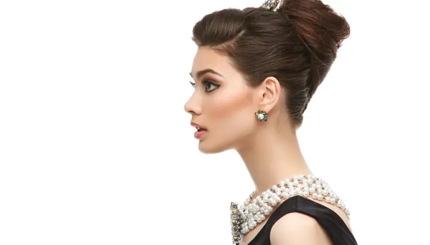 Elegante mujer con moño italiano, collar de perlas y pendientes llamativos.