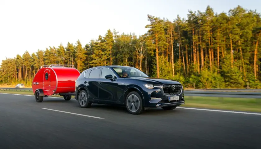 Ciemny SUV z czerwoną przyczepką typu teardrop jedzie po autostradzie. Zastanawiasz się, ile można jechać z przyczepką?
