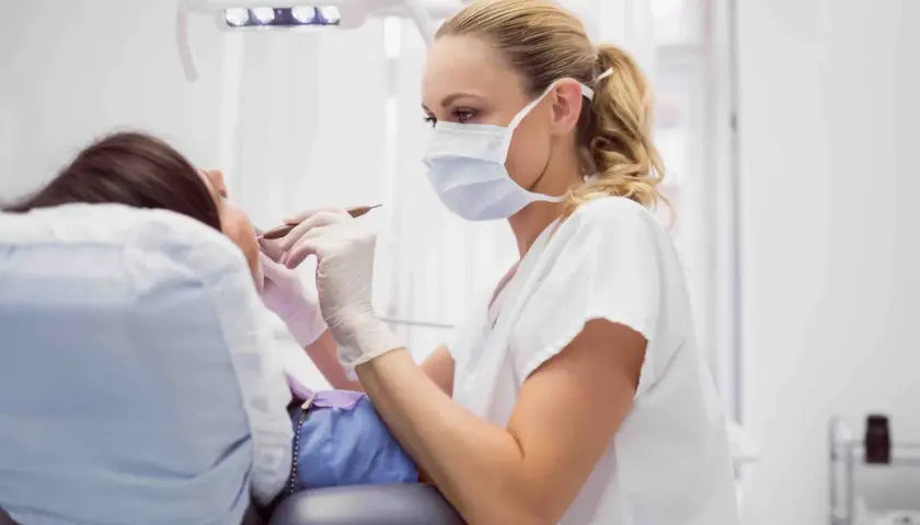 Dentista con mascherina esamina i denti di un paziente. La pulizia dei denti dura circa 30-60 minuti.