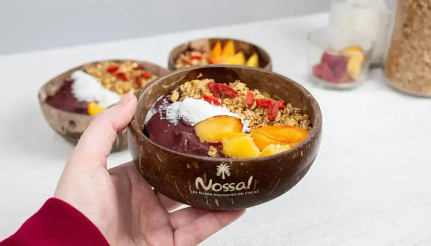 Une main tient un bol en noix de coco rempli d'un délicieux acai bowl, garni de fruits frais, de granola et de baies de goji.