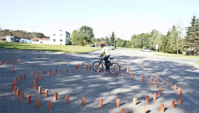 Osoba na rowerze w kamizelce odblaskowej i kasku manewruje między słupkami. To część testów na kartę rowerową.