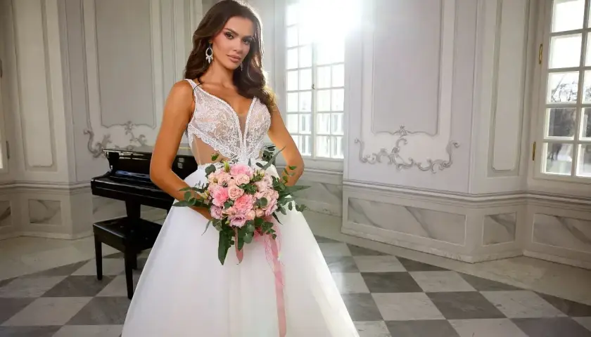 Elegancka panna młoda w koronkowej sukni z bukietem różowych kwiatów. Zastanawiasz się, ile kosztuje suknia ślubna?