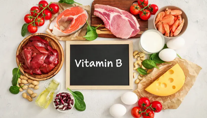 Tafel mit "Vitamin B" umgeben von Lebensmitteln wie Fisch, Fleisch, Eiern, Käse, Nüssen und Gemüse.