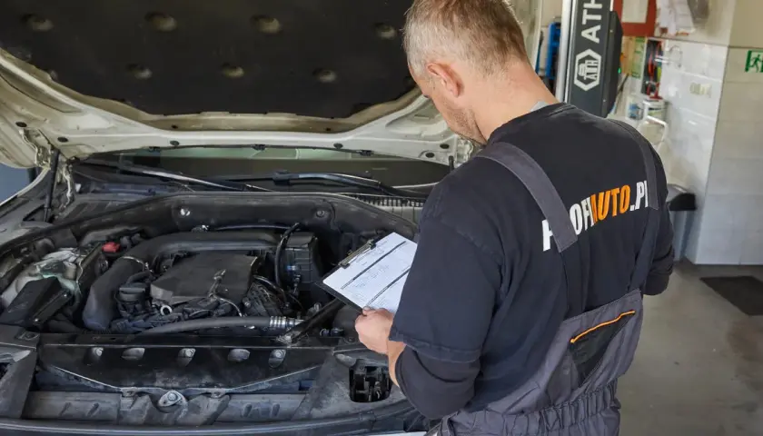 Mechanik sprawdza dokumentację przy otwartej masce samochodu. Czy wymiana oleju poza ASO a gwarancja to dobry pomysł?