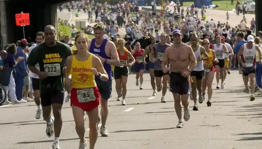 Uczestnicy biegną w maratonie, walcząc o jak najlepszy czas. Widać tłum biegaczy i kibiców.