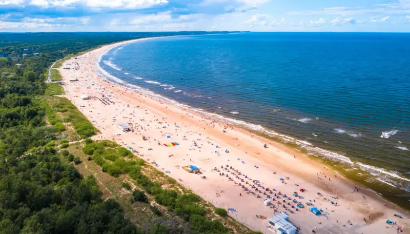 Słoneczne plaże nad morzem tętnią życiem. Tłumy plażowiczów odpoczywają na piasku, kąpią się w morzu i cieszą się wakacjami.