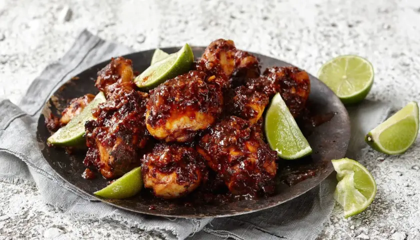 En tallrik med krispiga, klibbiga kycklingbitar, garnerad med limeklyftor.