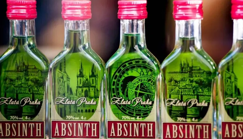 Fünf Flaschen grünen Absinths mit roten Kappen, jede mit einem Etikett, das Prag und die Aufschrift "Absinth" zeigt.