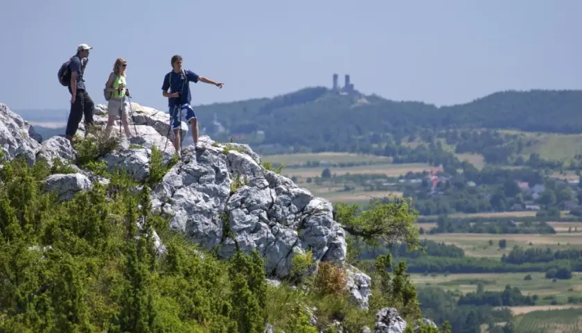 Trzech turystów na skale w Górach Świętokrzyskich, jeden wskazuje kierunek. W oddali widać ruiny zamku.