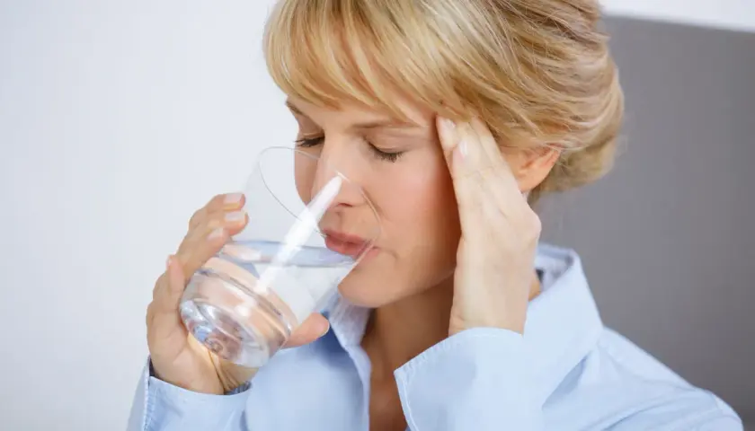 Frau mit Kopfschmerzen trinkt Wasser, hofft auf Linderung durch Magnesium.