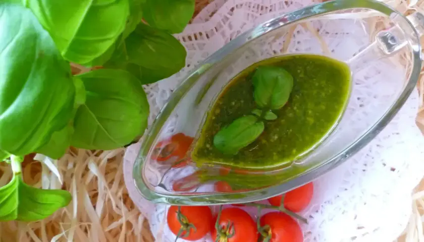 Aromatyczne pesto z bazylii w sosjerce, ozdobione listkami bazylii i pomidorkami koktajlowymi.