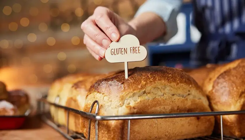 Dłoń wtyka tabliczkę "Gluten Free" w bochenek chleba. To przypomnienie, jak ważne jest, by wiedzieć, co robi gluten w organizmie, zwłaszcza przy wyborze pieczywa.