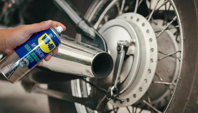 Mano che spruzza WD-40 su scarico cromato di moto. Un modo semplice per prendersi cura della cromatura e farla brillare.