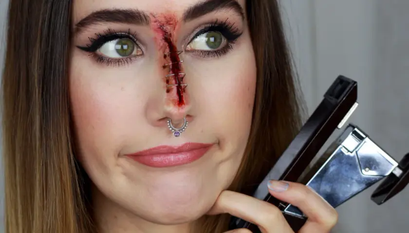 Sista minuten halloween sminkning: ett sår med häftklamrar på näsan, en häftapparat i handen.