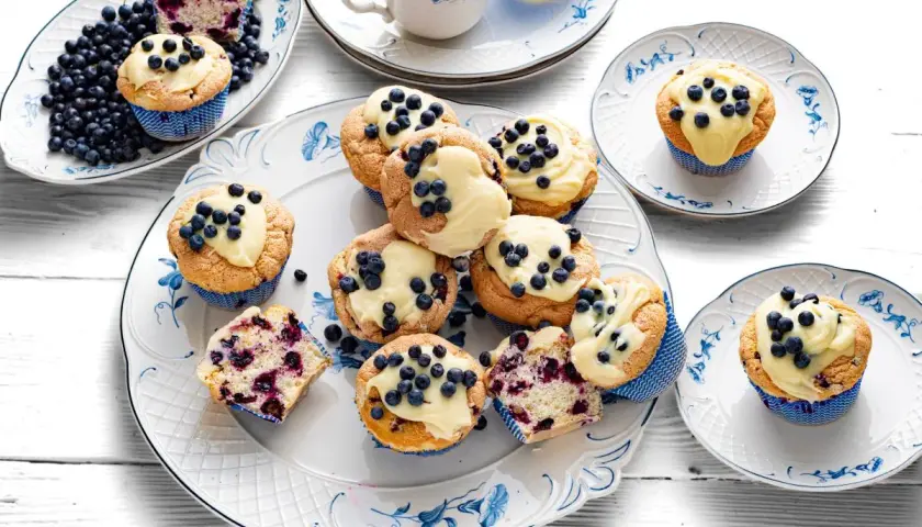 Pyszne muffiny z jagodami, udekorowane kremem i świeżymi owocami, kuszą swoim wyglądem i zapachem.