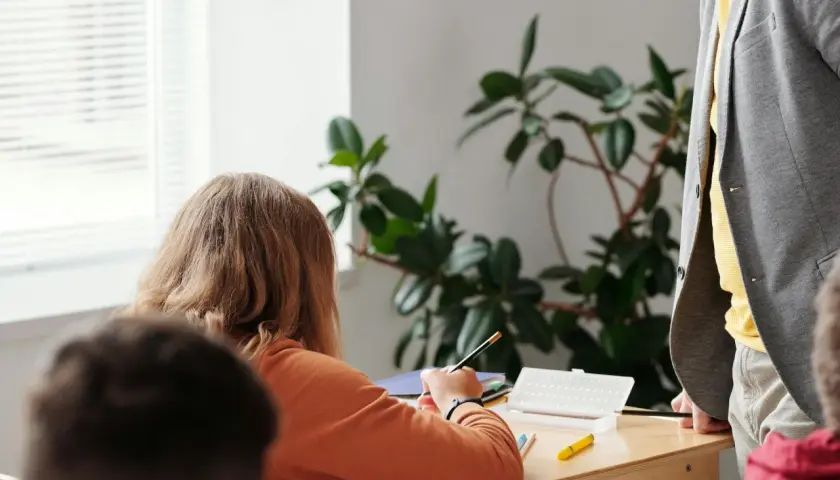 Ein Mädchen konzentriert sich auf seine Aufgaben während der Freiarbeit in der Grundschule. Ein Lehrer steht daneben.
